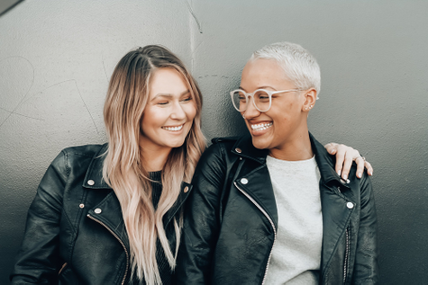 Two gal pals wearing leather jackets and smiling. 