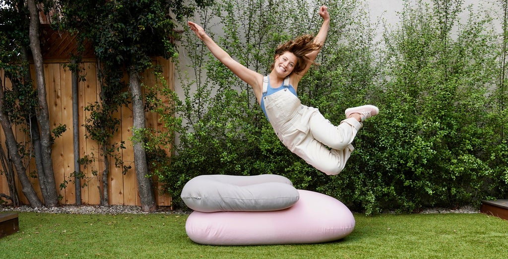 A woman jumping onto a stack of moon pod beanbag chairs. 
